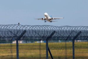 Razor wire security fence with an airplane taking off in the background.