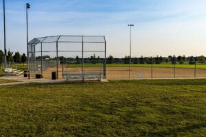 Chain-link backstop and fencing around a baseball field at dusk.