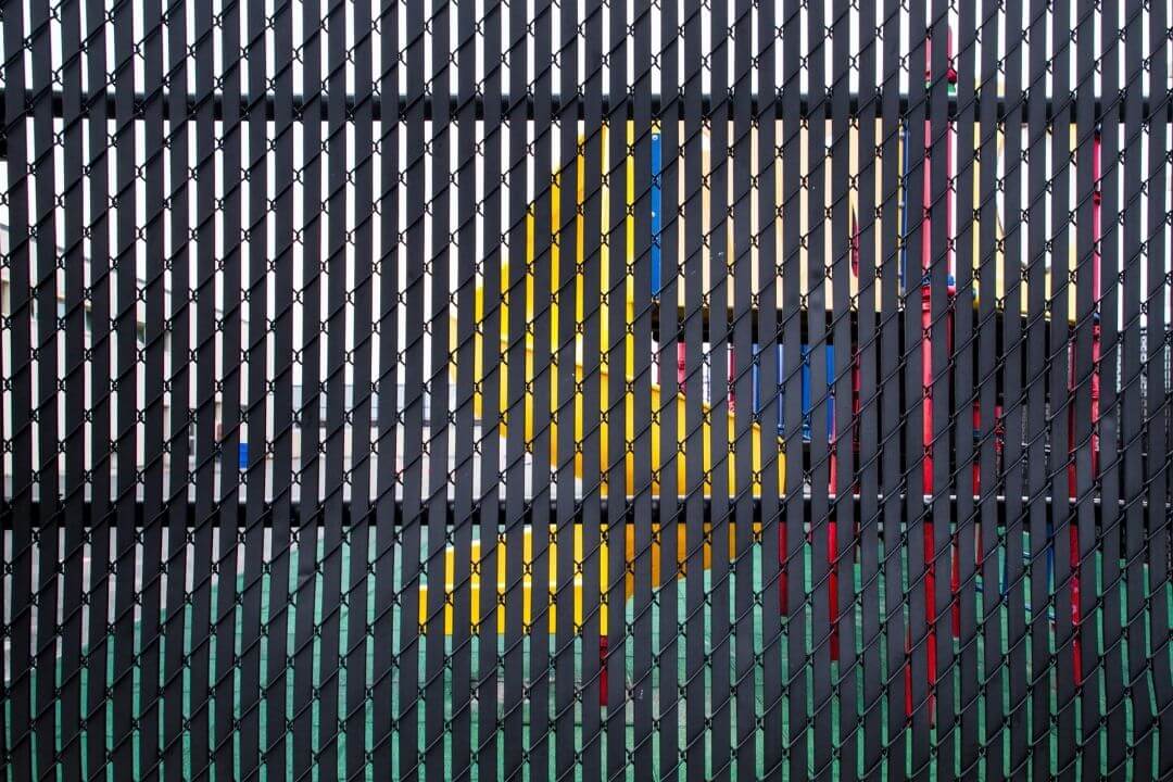 Black chain-link fence with slats revealing a colorful playground behind it