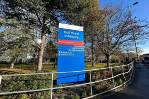 Hull Royal Infirmary hospital sign with directional arrows amid trees.