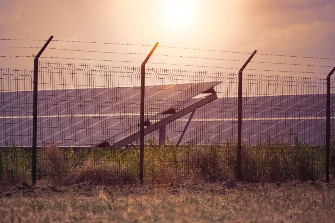 Barbed wire security fence surrounding a solar panel field at sunset.