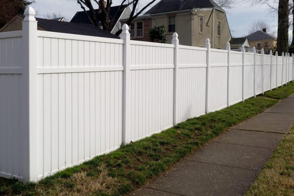 White vinyl privacy fence lining a sidewalk in a residential neighborhood.