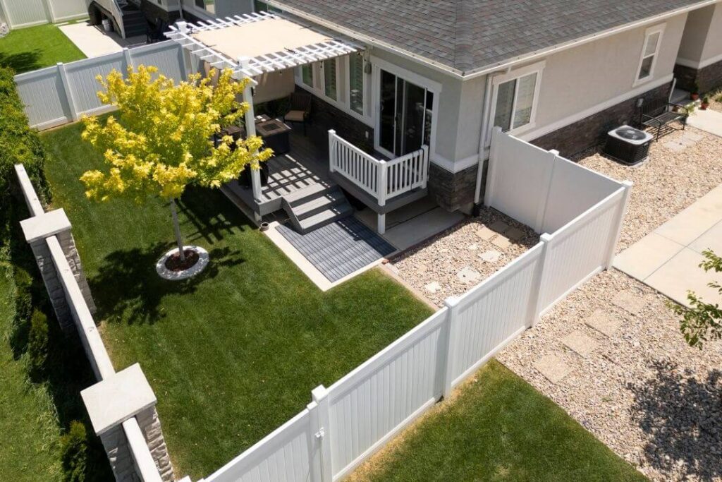 Aerial view of a backyard with white vinyl fencing, patio, and pergola.